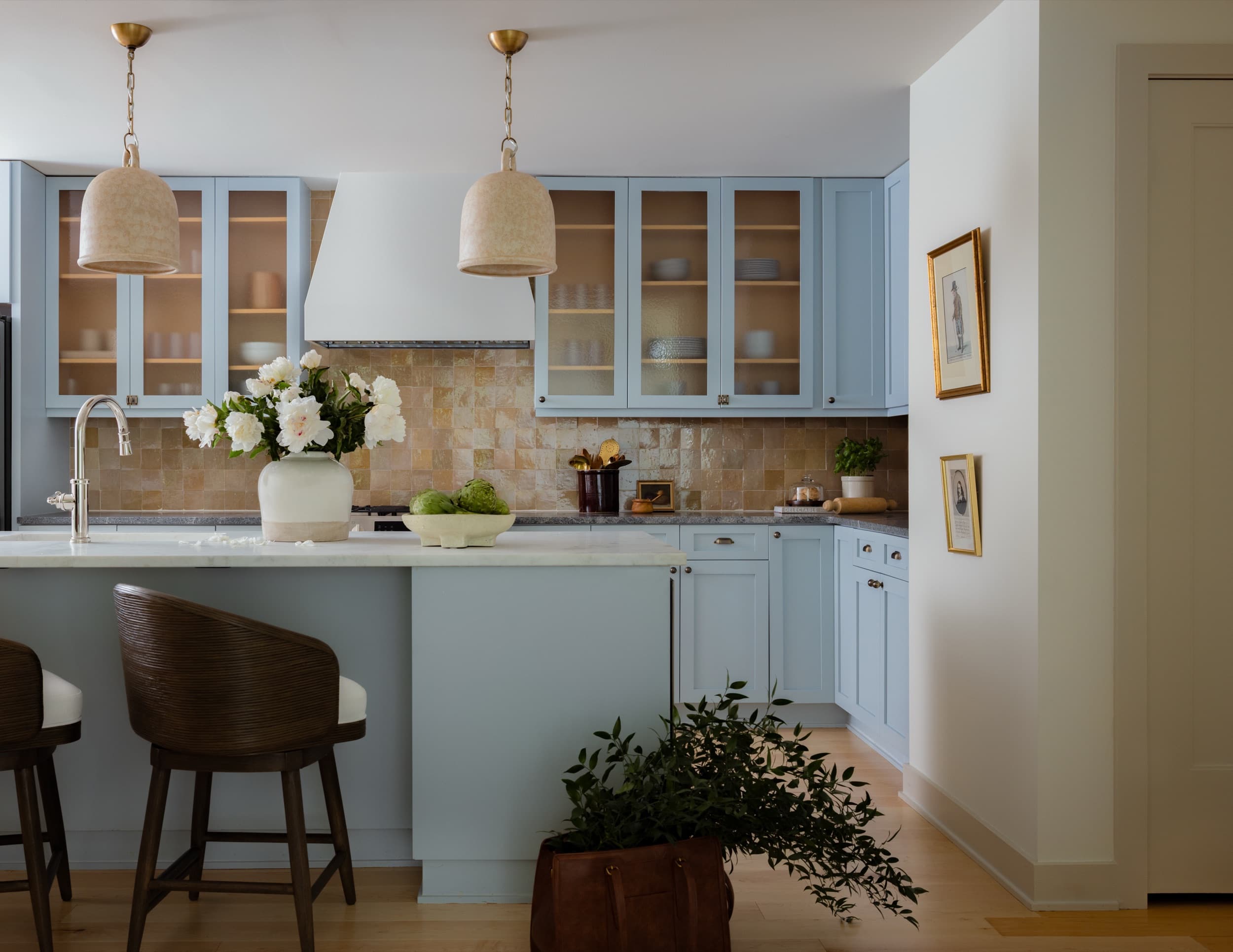 Kitchen with pale blue cabinetry, ceramic pendants on brass chains, a honey-toned zellige backsplash, and a white marble island