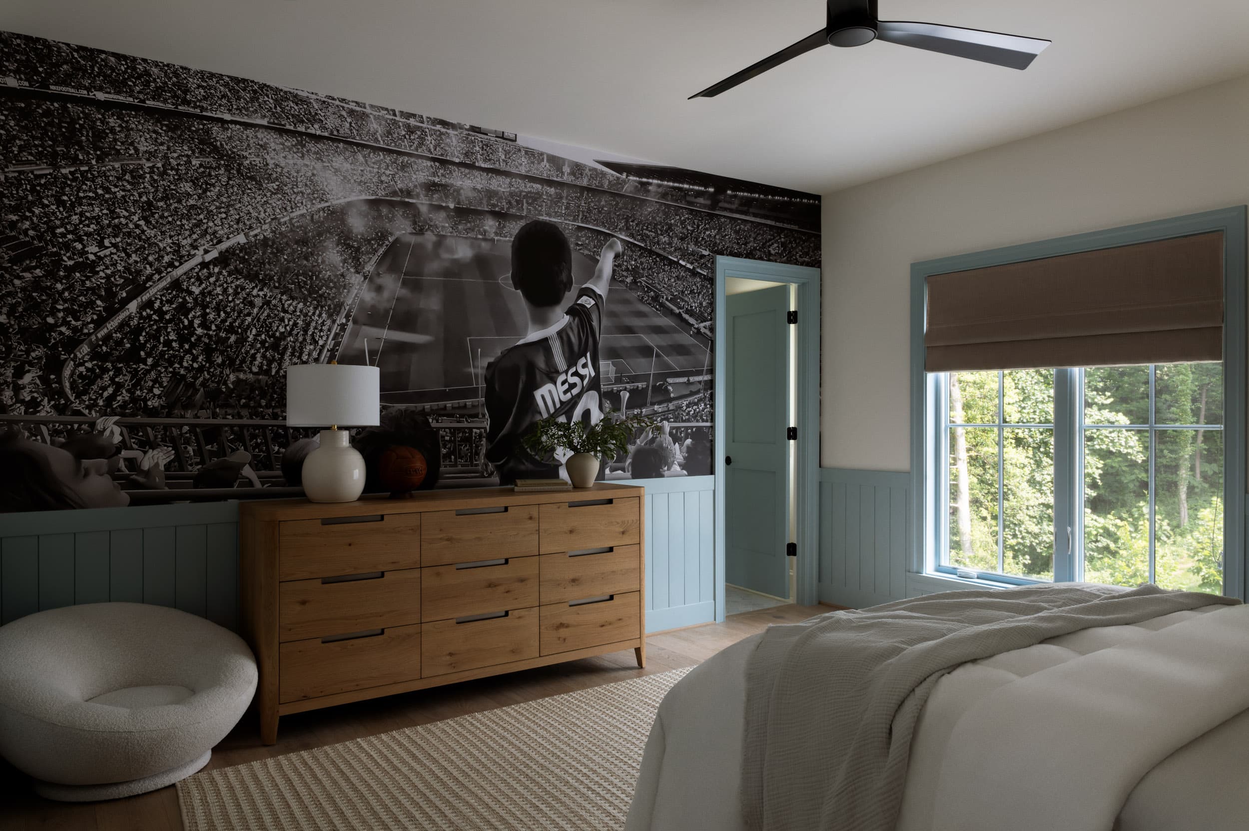 Boys bedroom with a black and white stadium mural, powder blue paneling, and an oak dresser