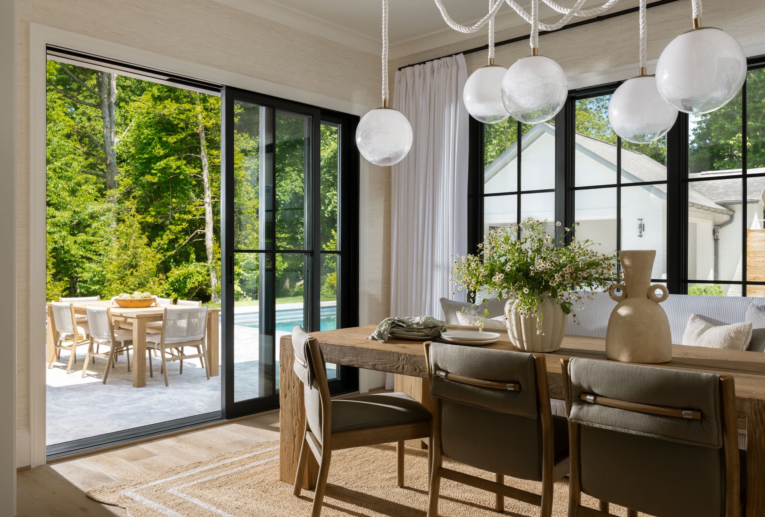 Dining room with a reclaimed oak table, glass globes hung on rope cords, and sliding doors open to the pool terrace