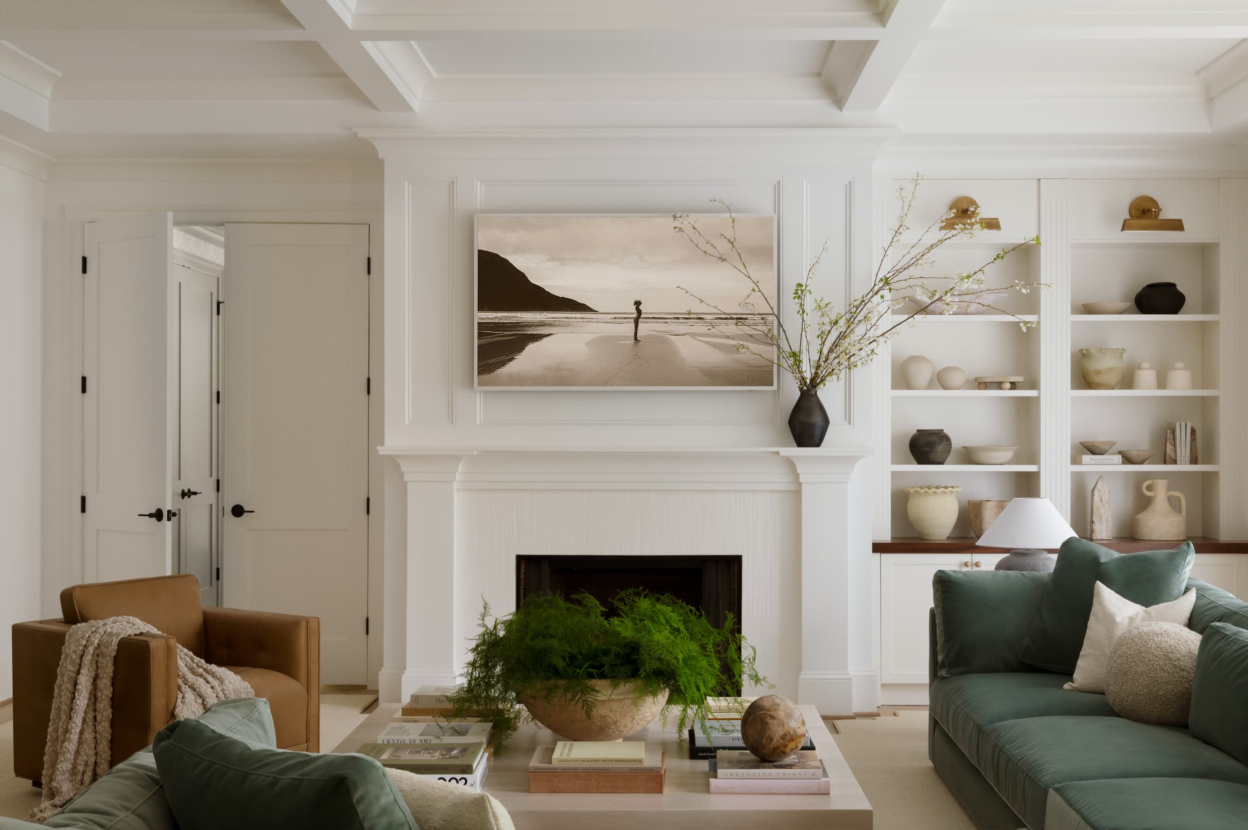 Living room with a coffered ceiling, green velvet sofas, a leather club chair, and styled built-ins beside the fireplace